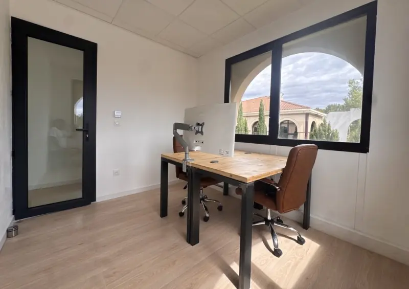 Bureau fermé à l’étage, deux postes face à face, vue sur le bâtiment à tuiles et les cyprès