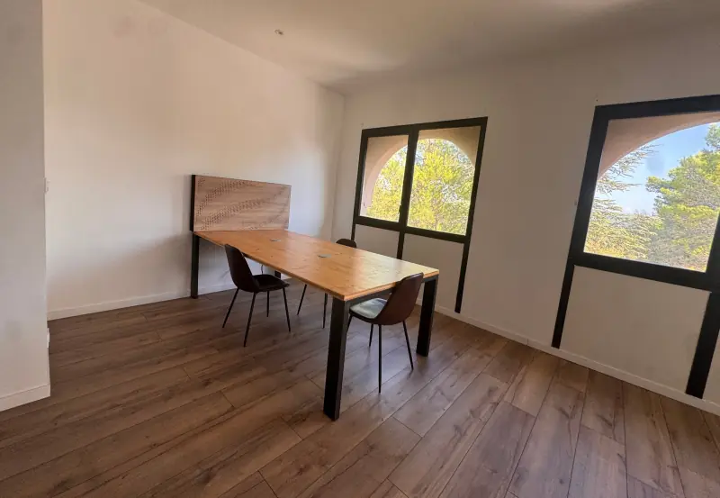 Bureau à l’étage avec grande table en bois et fenêtres cintrées sur les pins