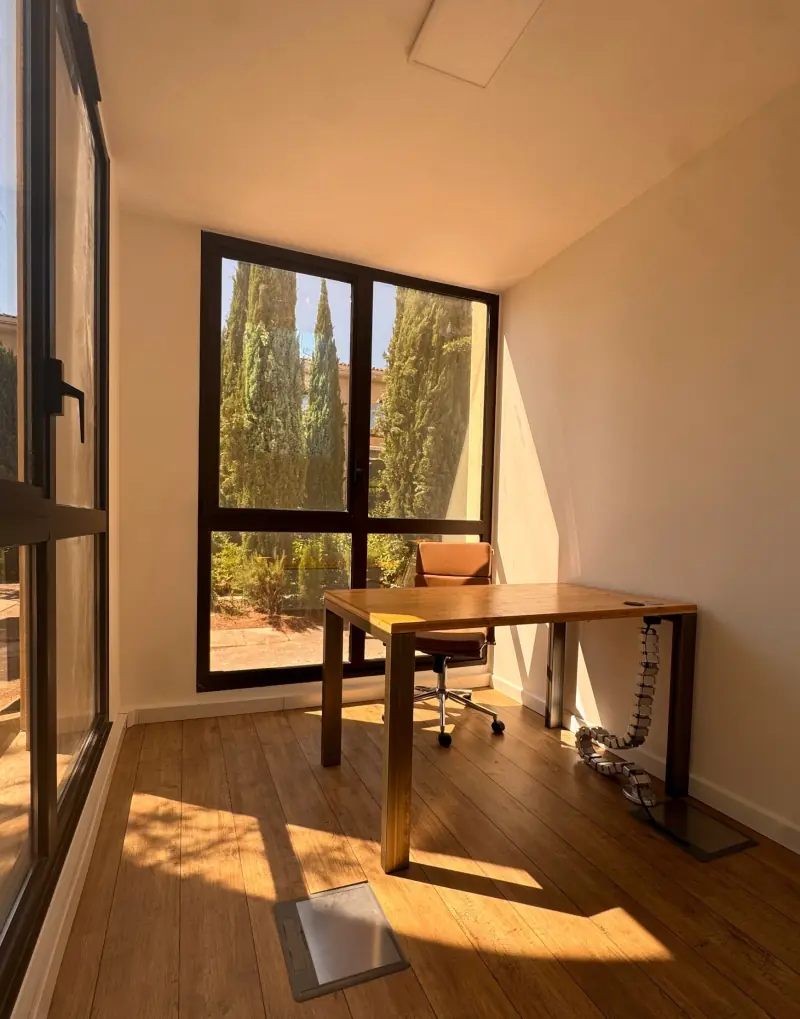 Bureau fermé en plein soleil, fauteuil camel et baie vitrée sur les cyprès