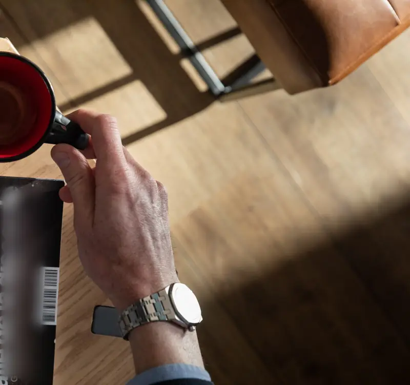 Une tasse de café rouge à la main, sur la table en bois
