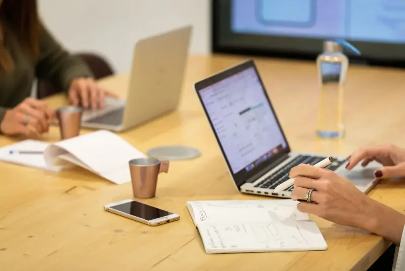 Deux coworkers sur leurs ordinateurs portables autour d’une table en bois