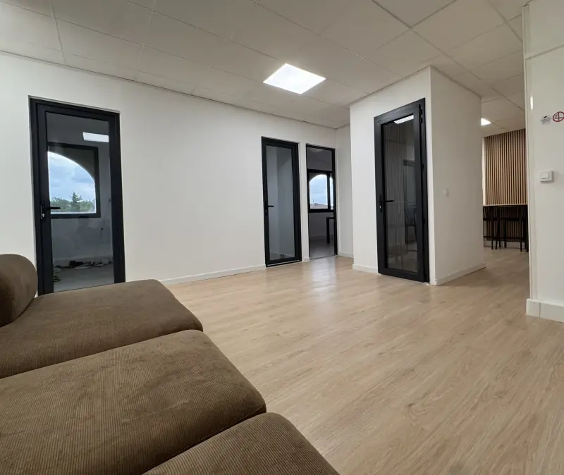 Espace commun, canapé en velours et portes vitrées noires des bureaux