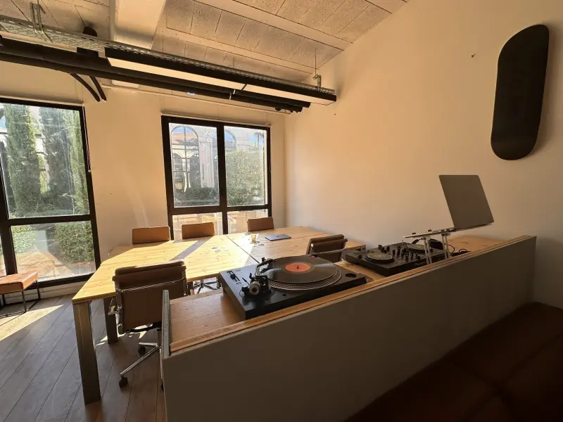 Grande table en bois et platines vinyle devant les fenêtres de l’open space