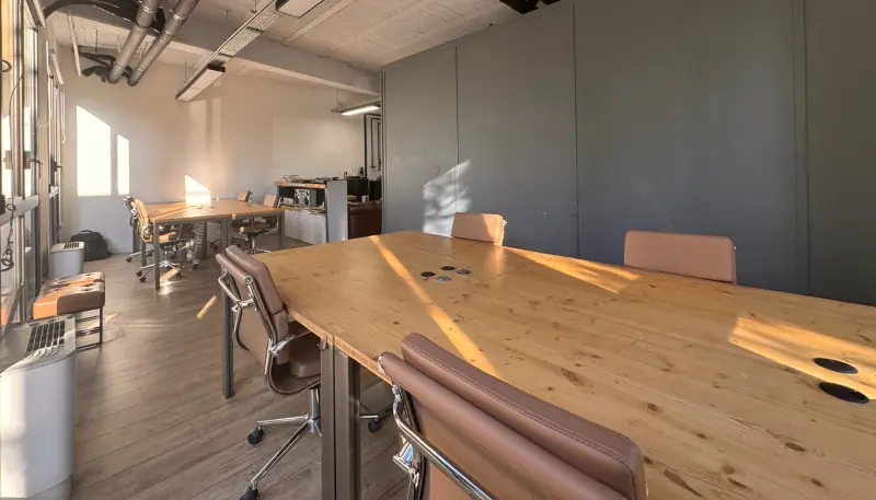 Grande table en bois au soleil et fauteuils en cuir camel dans l’open space