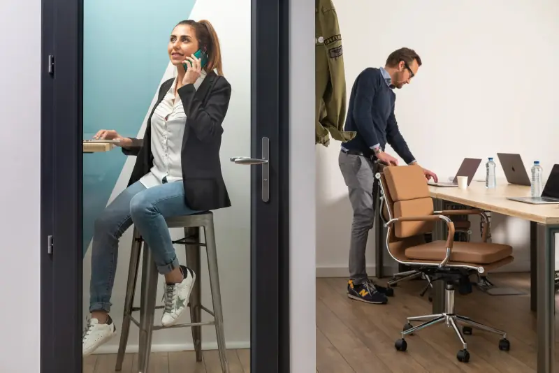 Une coworkeuse au téléphone dans la phone box, un coworker à son bureau