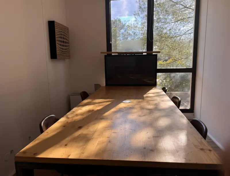 Salle de réunion en plein soleil, table en bois et baie vitrée sur les pins